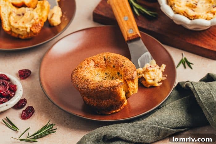A rosemary popover on a plate with a knife with butter.