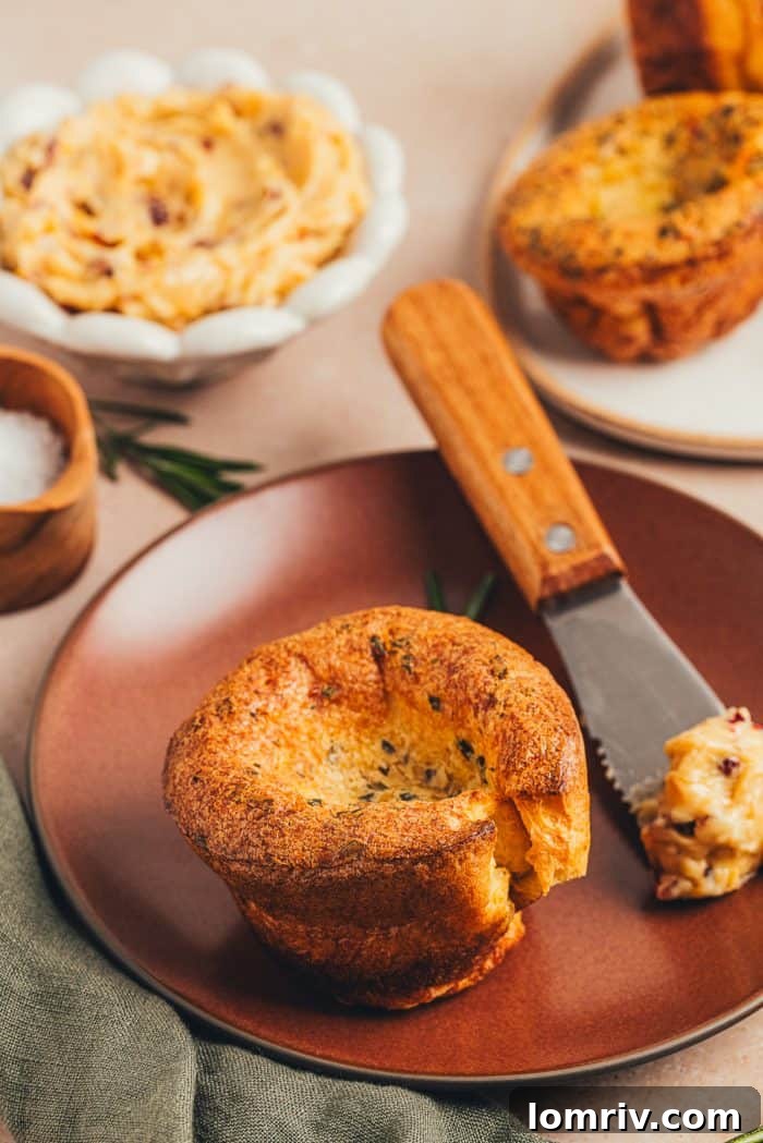 A rosemary popover on a plate with a knife with butter.