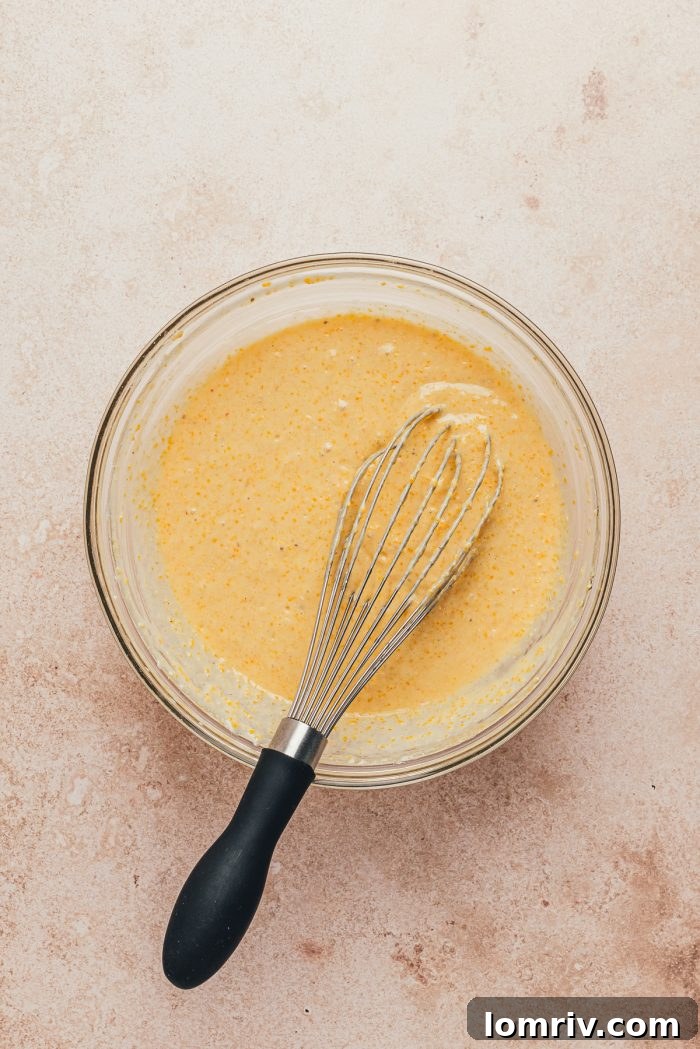 A glass bowl with the cornbread batter and a whisk.