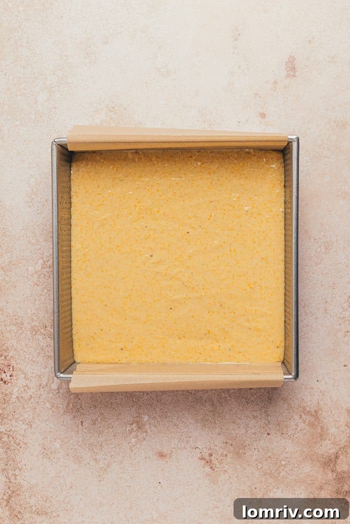 A baking pan with parchment paper and cornbread batter.
