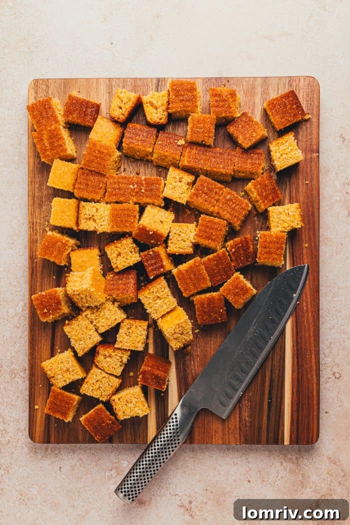 Cornbread cut into cubes on a wooden cutting board with a large knife.