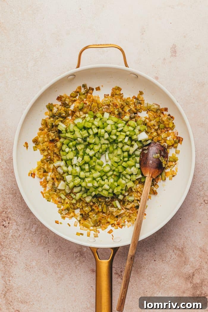 Caramelized leeks and diced celery in a white skillet with a wooden spoon.