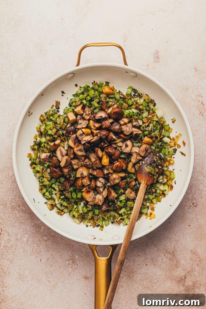 A white skillet with leeks, celery, garlic, herbs, chestnuts, and a wooden spoon.