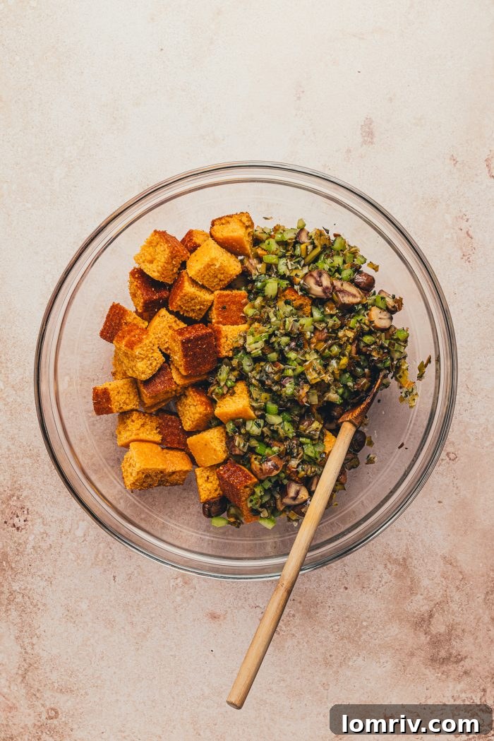 A glass bowl with dried out cornbread cubes and the cooked vegetable mixture.