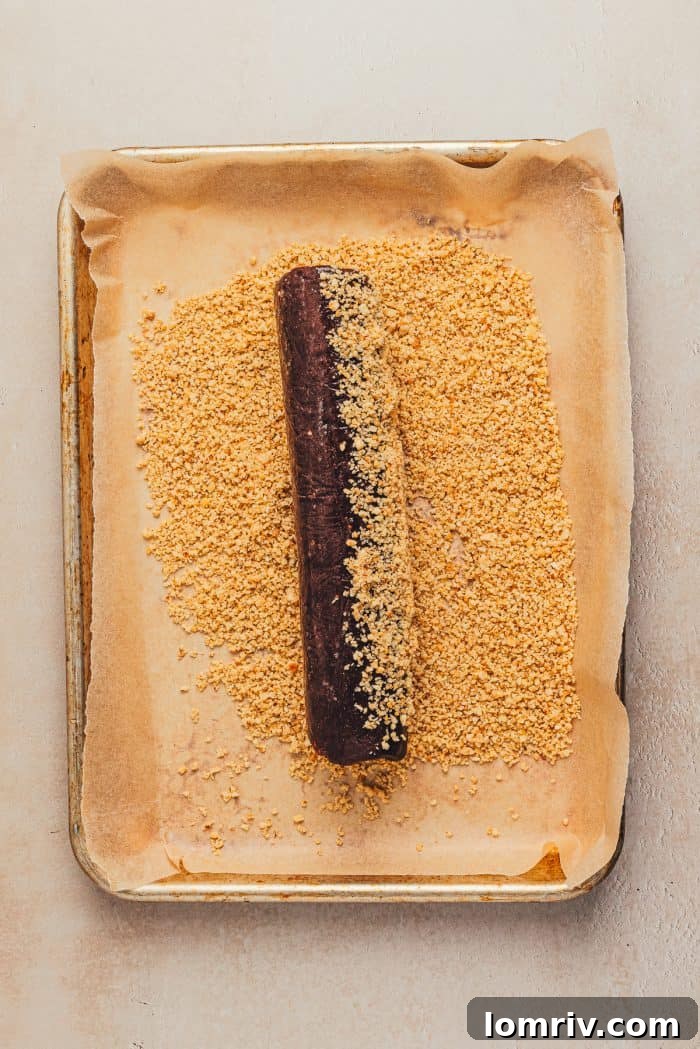 A chilled cookie dough log being rolled in finely chopped hazelnuts for a beautiful coating.