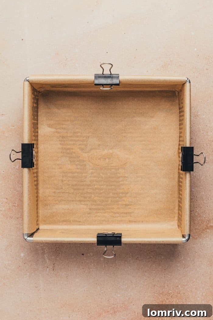 An 8-inch square baking pan meticulously lined with parchment paper, leaving an overhang for easy removal.