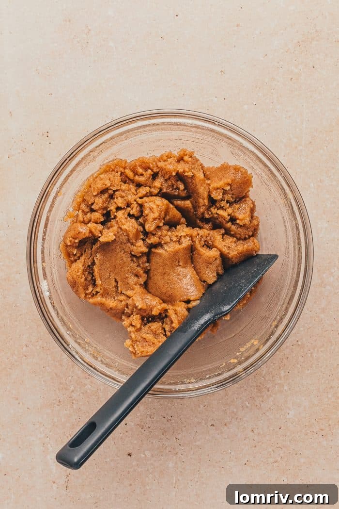 A glass bowl filled with the crumb topping mixture, showing its coarse, textured consistency, alongside a spatula.