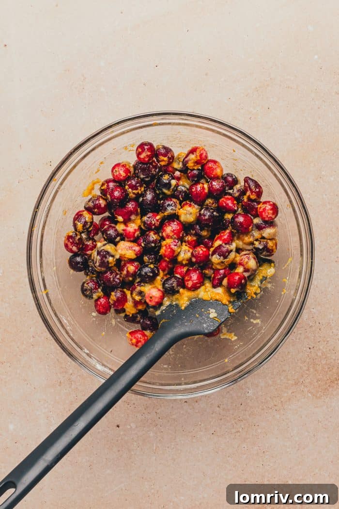A bowl containing fresh cranberries coated with orange zest, flour, and sugar, ready to be layered in the cake.