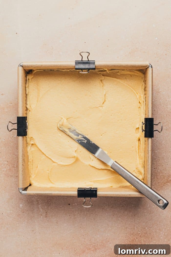 A square baking pan lined with parchment paper, holding a smooth, even layer of unbaked cake batter.