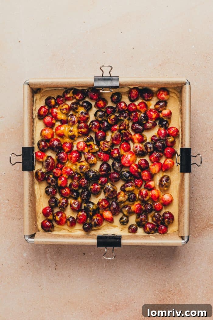 A baking pan filled with the unbaked cake batter, topped with a generous layer of vibrant cranberry mixture.