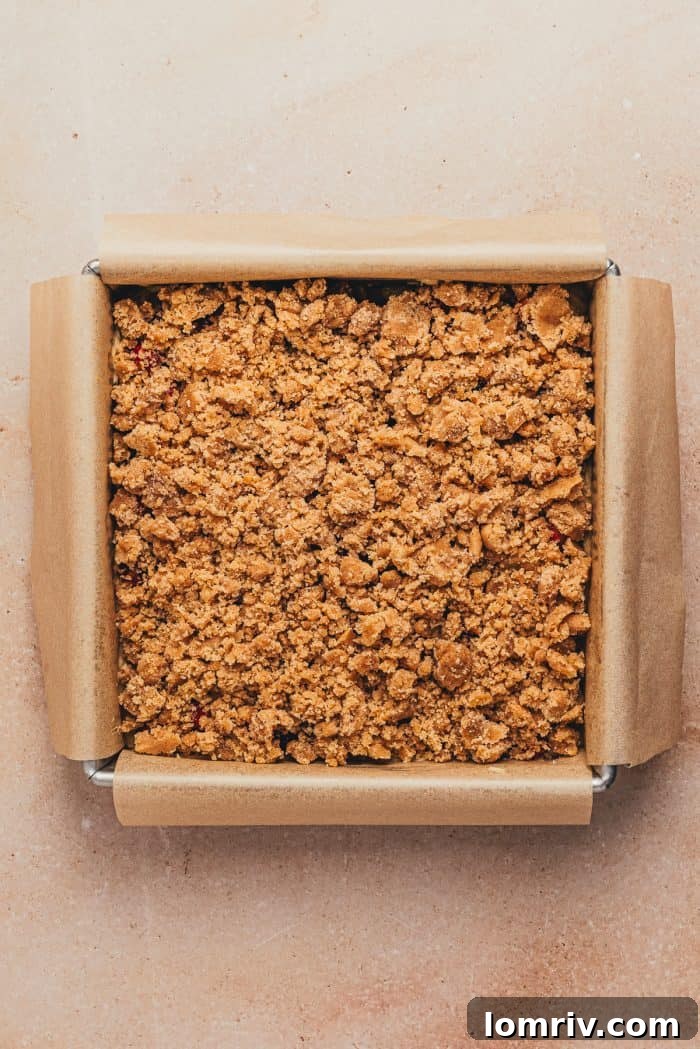 A square cake pan containing the unbaked cranberry crumb cake, beautifully layered with batter, cranberries, and a generous streusel topping.