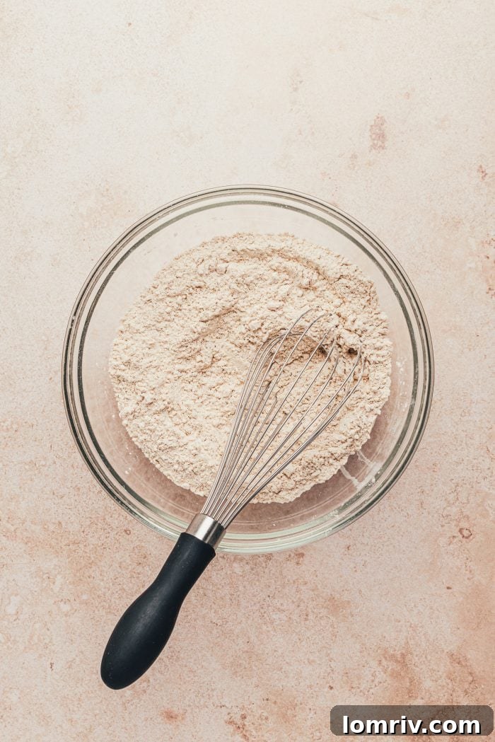 A glass bowl with the dry ingredients mixed together and a whisk.