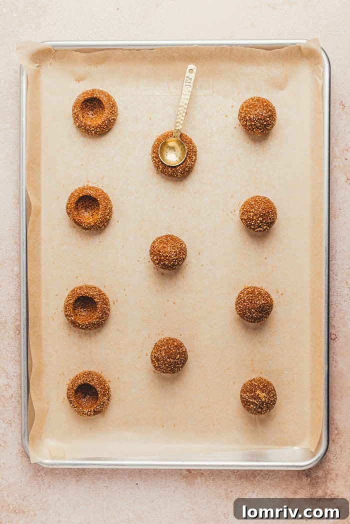 The thumbprint cookie dough placed on cookie sheets with a spoon being used to create the thumbprint.