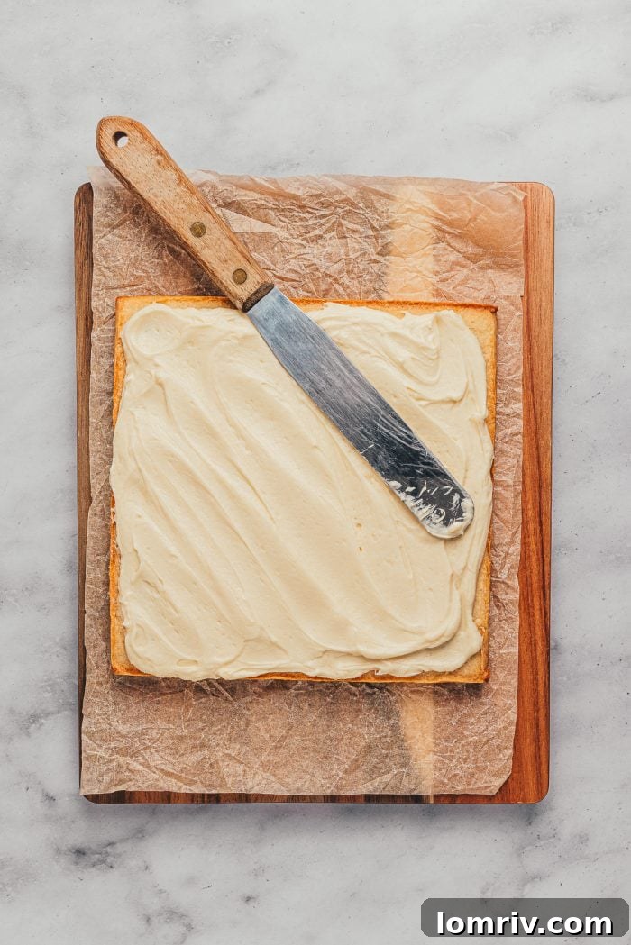 Baked sugar cookie bars on a wooden cutting board with the frosting being spread over the top.