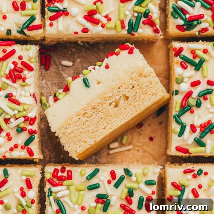 Frosted sugar cookie bars sliced showing the top of the bar with sprinkles. One bar is flipped on its side showing the bar and the thick frosting.