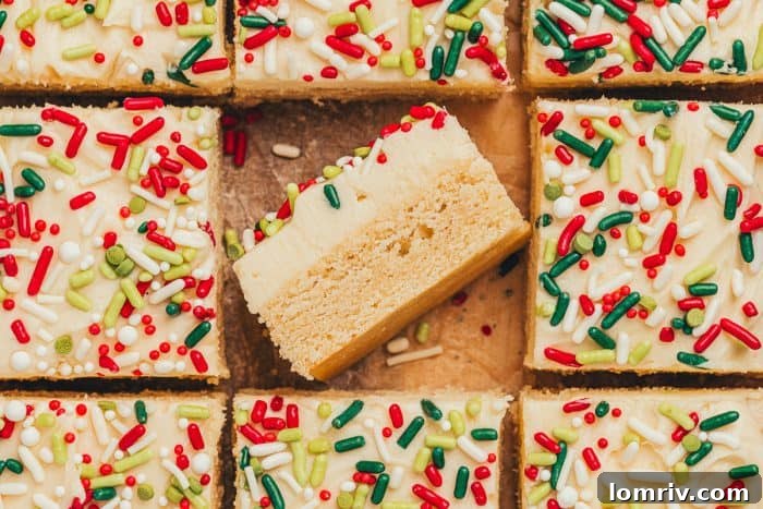 Frosted sugar cookie bars sliced showing the top of the bar with sprinkles. One bar is flipped on its side showing the bar and the thick frosting.