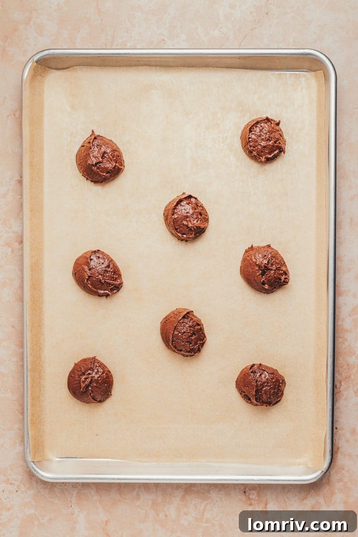 Individual scoops of chocolate whoopie pie batter perfectly spaced on a parchment-lined baking sheet, ready for baking.