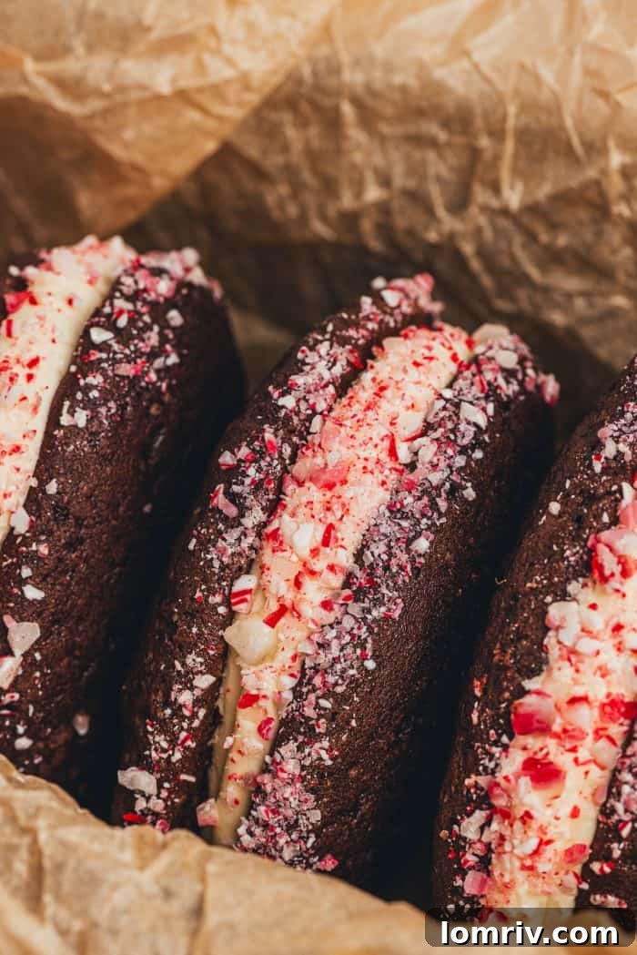 Three perfectly crafted chocolate peppermint whoopie pies, showcasing the creamy filling and crushed candy cane coating.