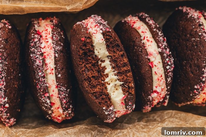 A perfectly arranged row of four chocolate peppermint whoopie pies, highlighting their creamy filling and crushed peppermint edges.