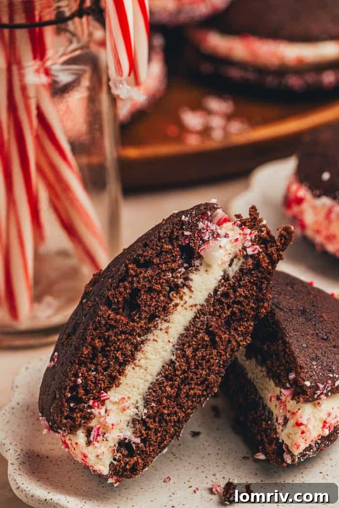 A chocolate peppermint whoopie pie cut in half, revealing the creamy white chocolate peppermint filling, with candy canes in the background.