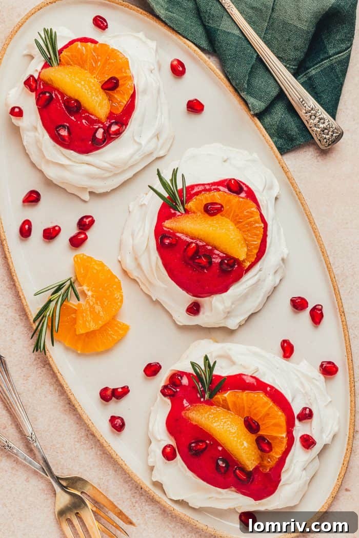 Three mini pavlovas with vibrant cranberry curd, fresh orange slices, and glistening pomegranate seeds on a white platter, ready for a festive celebration.
