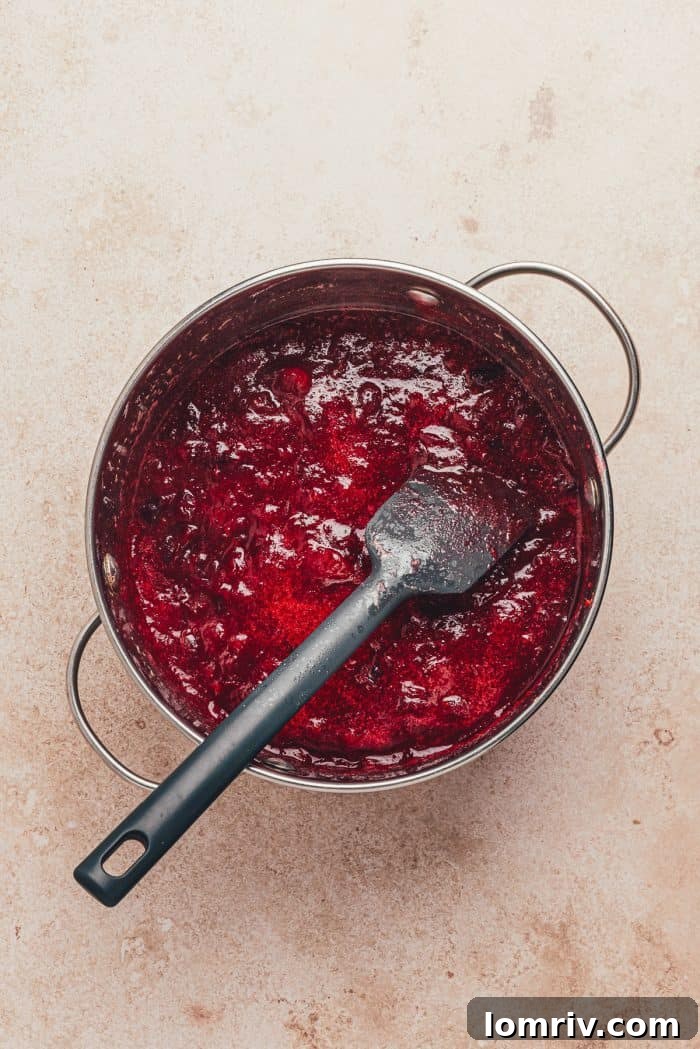 Fresh cranberries simmering in a saucepan with a spatula, creating the base for the cranberry curd.