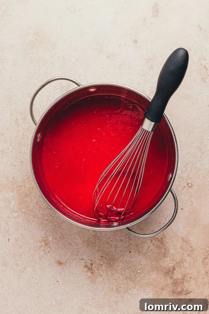 Smooth, blended cranberry sauce in a saucepan, being whisked to incorporate additional ingredients for the curd.