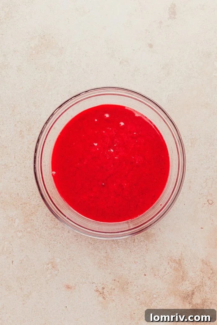 Vibrant cranberry curd cooling in a glass mixing bowl, showcasing its rich texture and color.