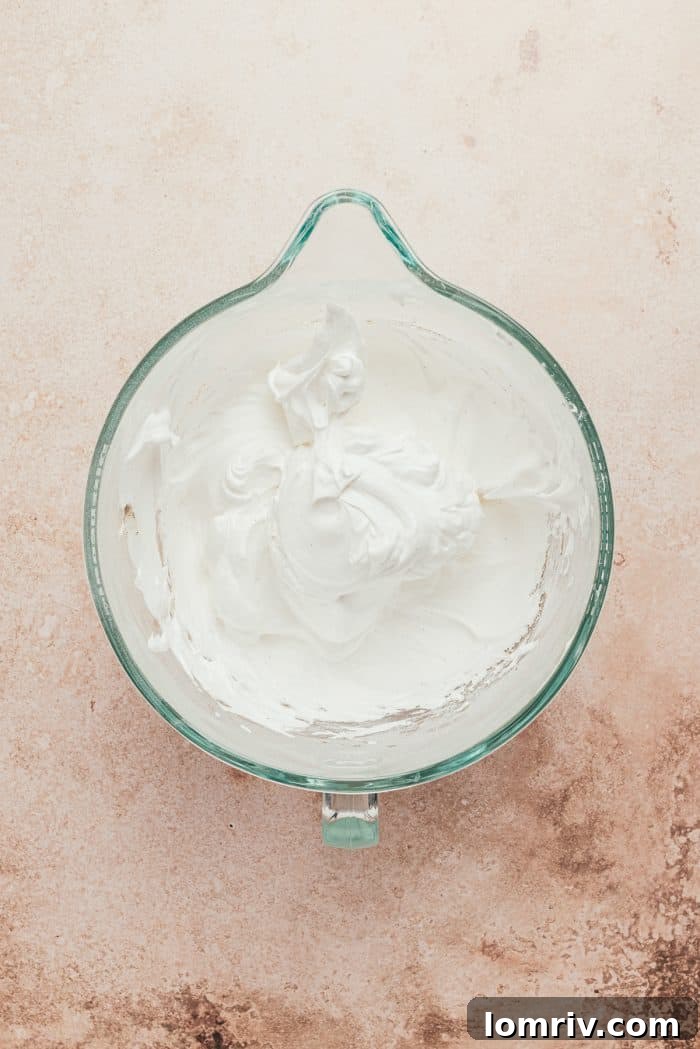 A glass mixing bowl containing perfectly whipped meringue, glossy and stiff, ready to be piped.