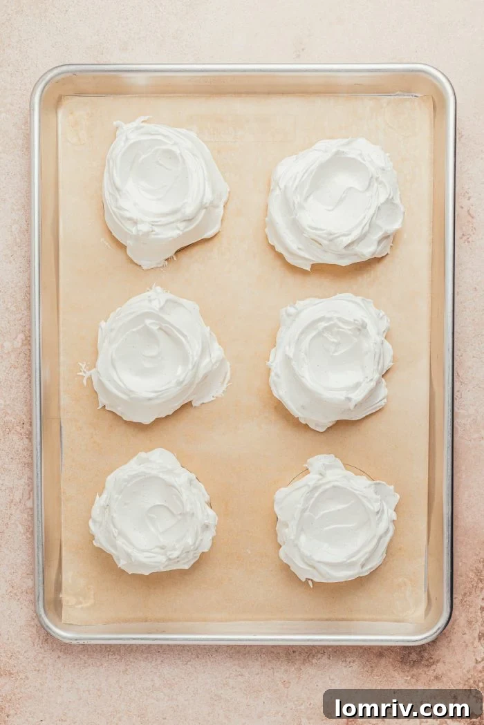 Unbaked mini pavlovas, shaped into mounds with indentations, arranged on a baking sheet lined with parchment paper.