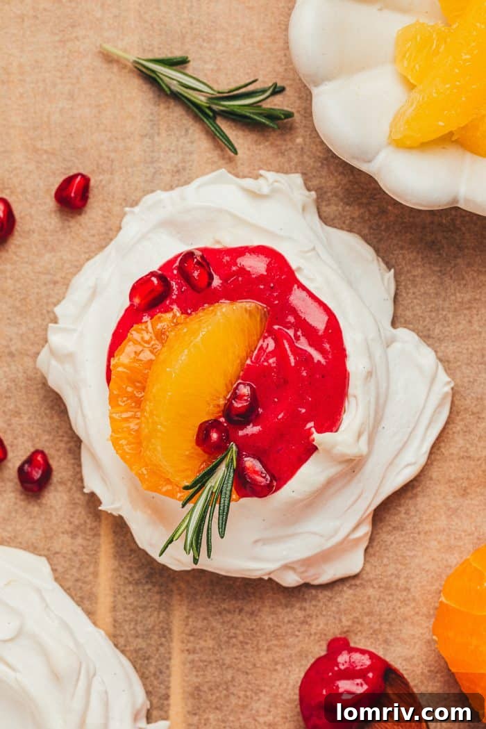 A beautifully assembled mini pavlova with cranberry curd, vibrant orange slices, and glistening pomegranate seeds on a white platter.