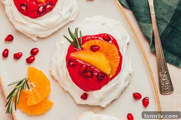 Two exquisitely prepared mini pavlovas, featuring cranberry curd, fresh orange slices, and festive garnishes, presented on a white serving platter.