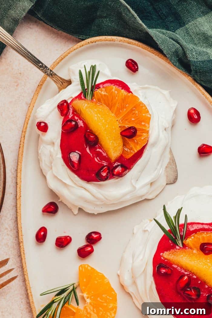 Two perfectly crafted mini pavlovas adorned with rich cranberry curd, vibrant orange slices, and festive garnishes, presented on a platter with a serving spatula.