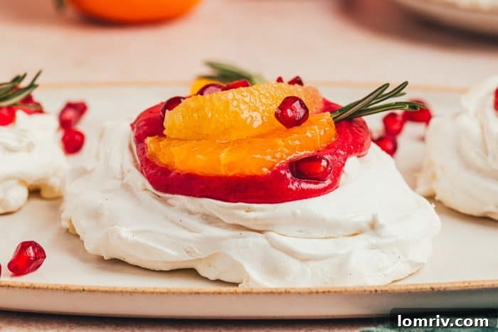A close-up shot of a mini pavlova generously filled with vibrant cranberry curd, garnished with fresh orange slices and pomegranate seeds.