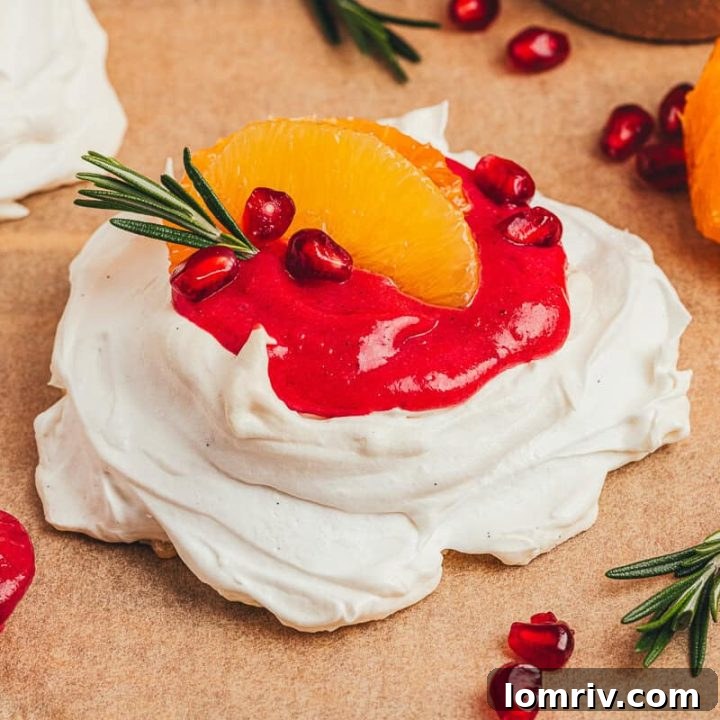 A beautifully garnished mini pavlova with cranberry curd, orange slices, and rosemary sprigs.