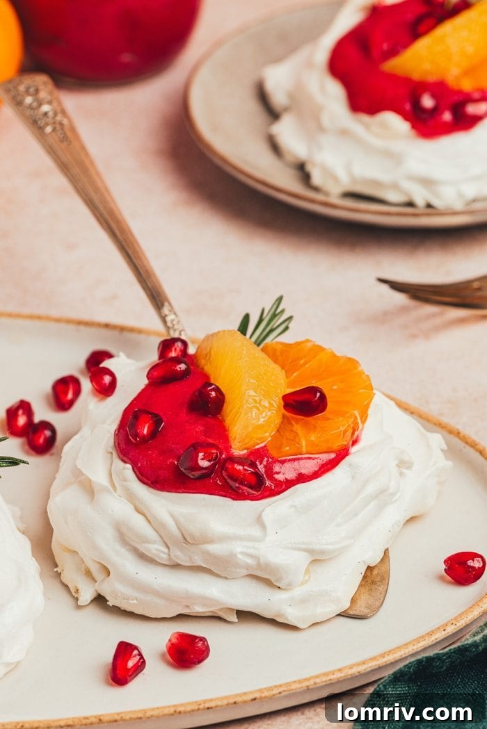 A close-up of a single mini pavlova with a generous swirl of cranberry curd, fresh orange segments, and deep red pomegranate seeds, ready to be enjoyed.