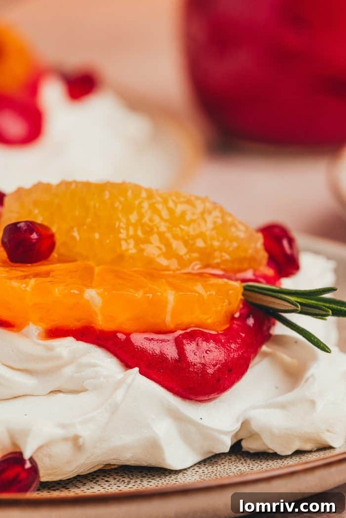 A pristine mini pavlova, topped with luscious cranberry curd and garnished with orange slices and pomegranate arils, showcased on a white background.