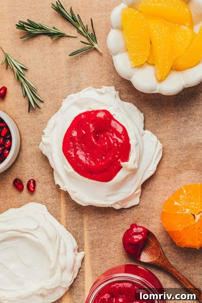 One mini pavlova filled with cranberry curd and garnished, next to an unfilled mini pavlova shell, showcasing the difference before and after filling.