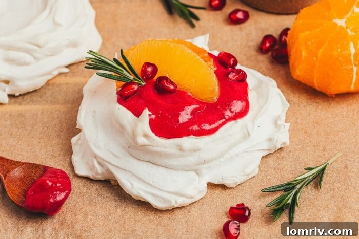 A beautifully decorated mini pavlova, filled with cranberry curd and adorned with orange slices and pomegranate, on a white plate.
