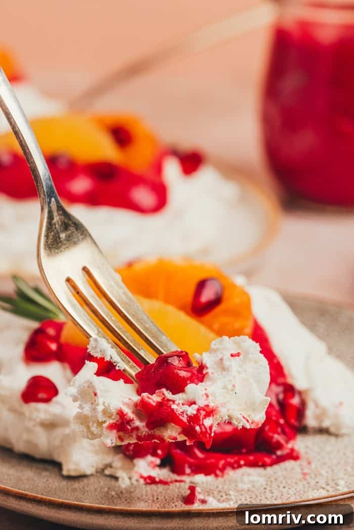 A fork taking a delicious bite out of a mini pavlova, revealing its soft interior and the rich cranberry curd, with orange slices and pomegranate nearby.
