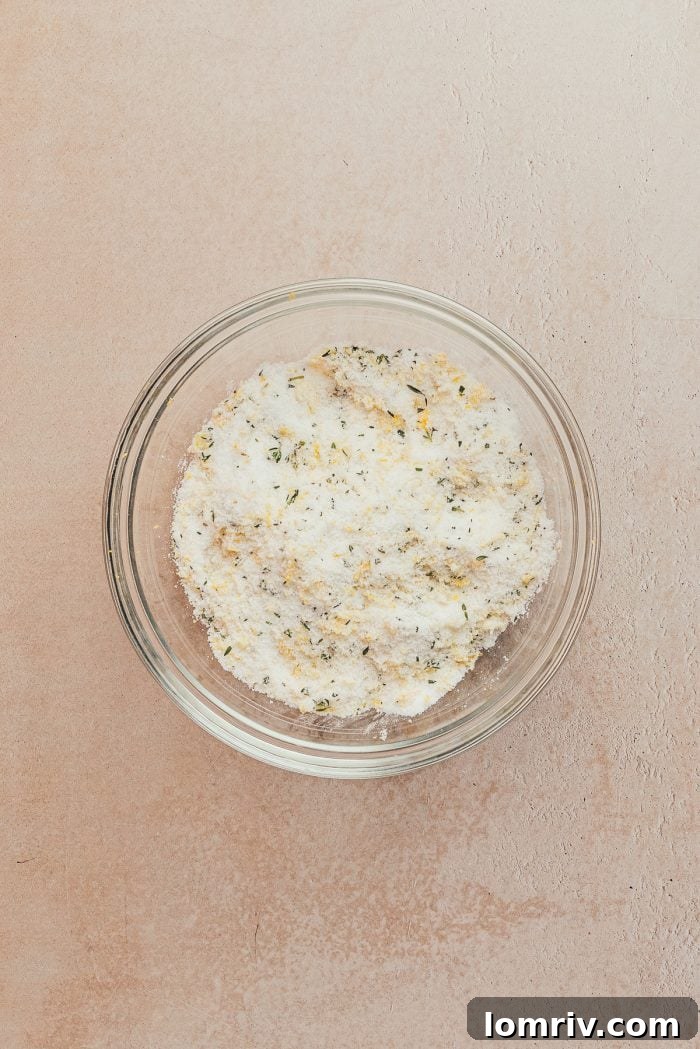 A glass bowl containing a vibrant mixture of fresh lemon zest and granulated sugar, ready for the next step in baking.