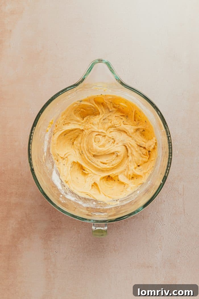 A glass mixing bowl containing the creamy, unbaked lemon pound cake batter, showcasing its smooth texture.