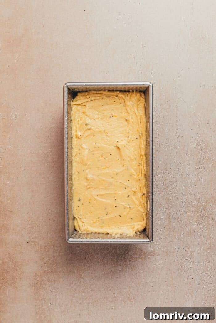 An unbaked lemon pound cake batter, perfectly smoothed, resting within a tin loaf pan, ready to go into the oven.