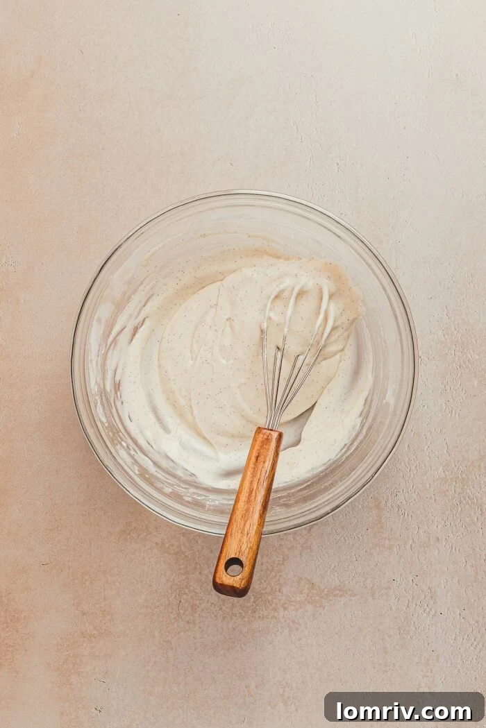 A glass bowl holds the luscious lemon icing, with a whisk resting inside, ready for drizzling over the cake.