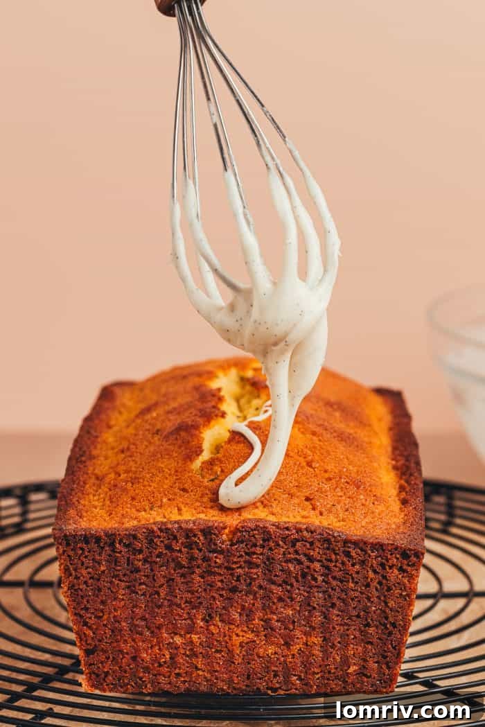A whisk gently drizzles thick, creamy icing over the top of a lemon thyme pound cake, creating beautiful cascades.