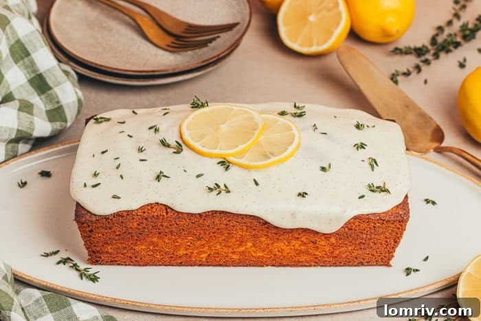 A beautifully baked lemon Thyme cake loaf rests on a white platter, ready to be sliced and served.