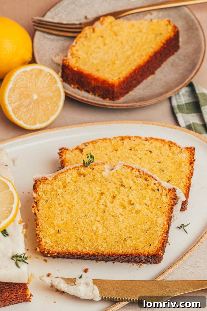 Two generous slices of lemon pound cake are elegantly presented on a white plate, with fresh lemons cut in half forming a vibrant backdrop.