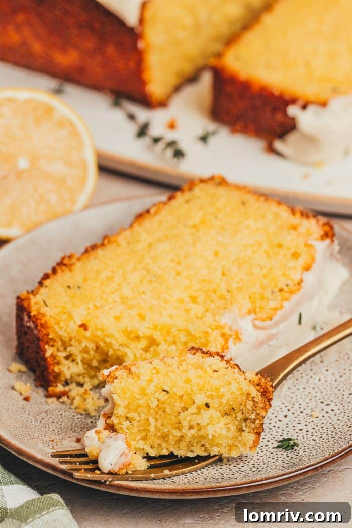A tempting slice of lemon thyme loaf cake on a white plate, with a fork poised to take a bite, highlighting the moist texture and glaze.
