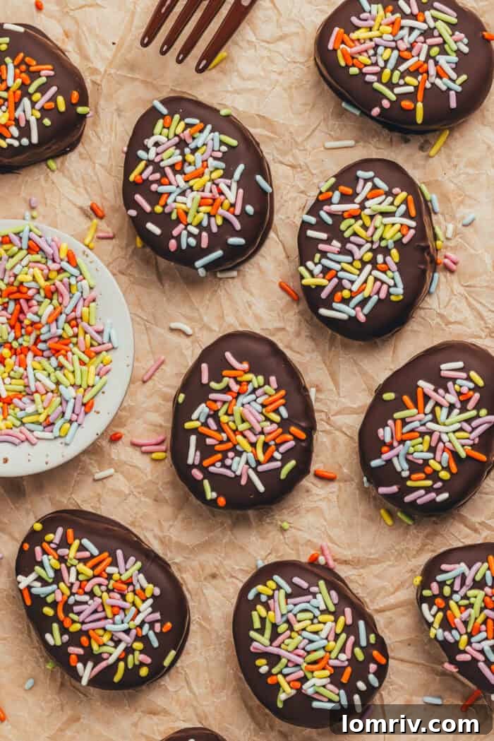 A few homemade chocolate Easter eggs scattered on parchment paper with a small plate filled with sprinkles.