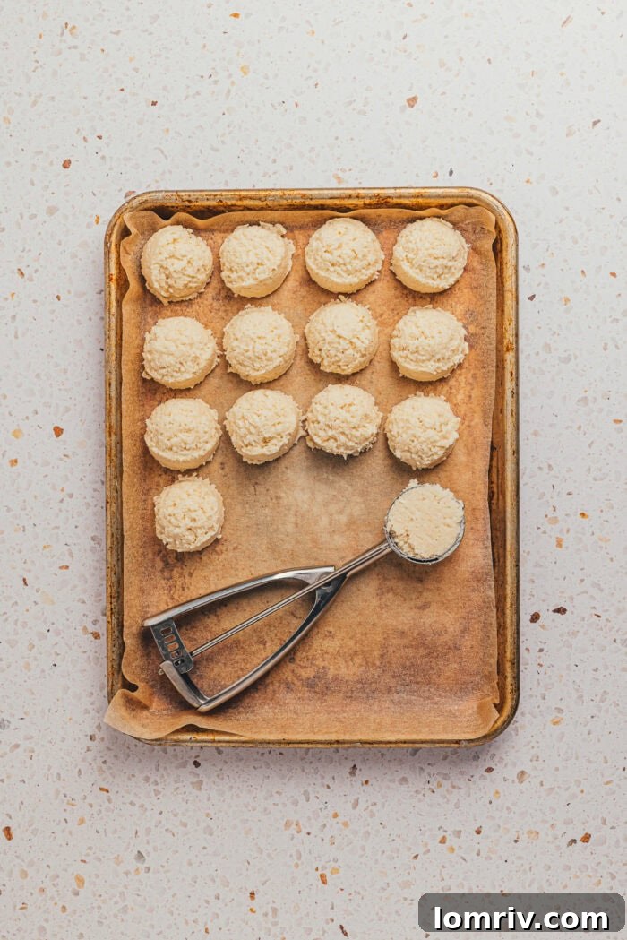 The coconut filling balls are placed on a baking sheet with parchment paper and a scoop.